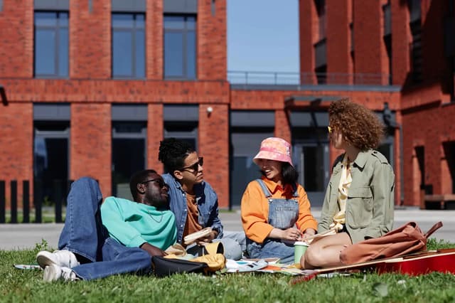 Students relaxing together on the grass outside a red-brick university building